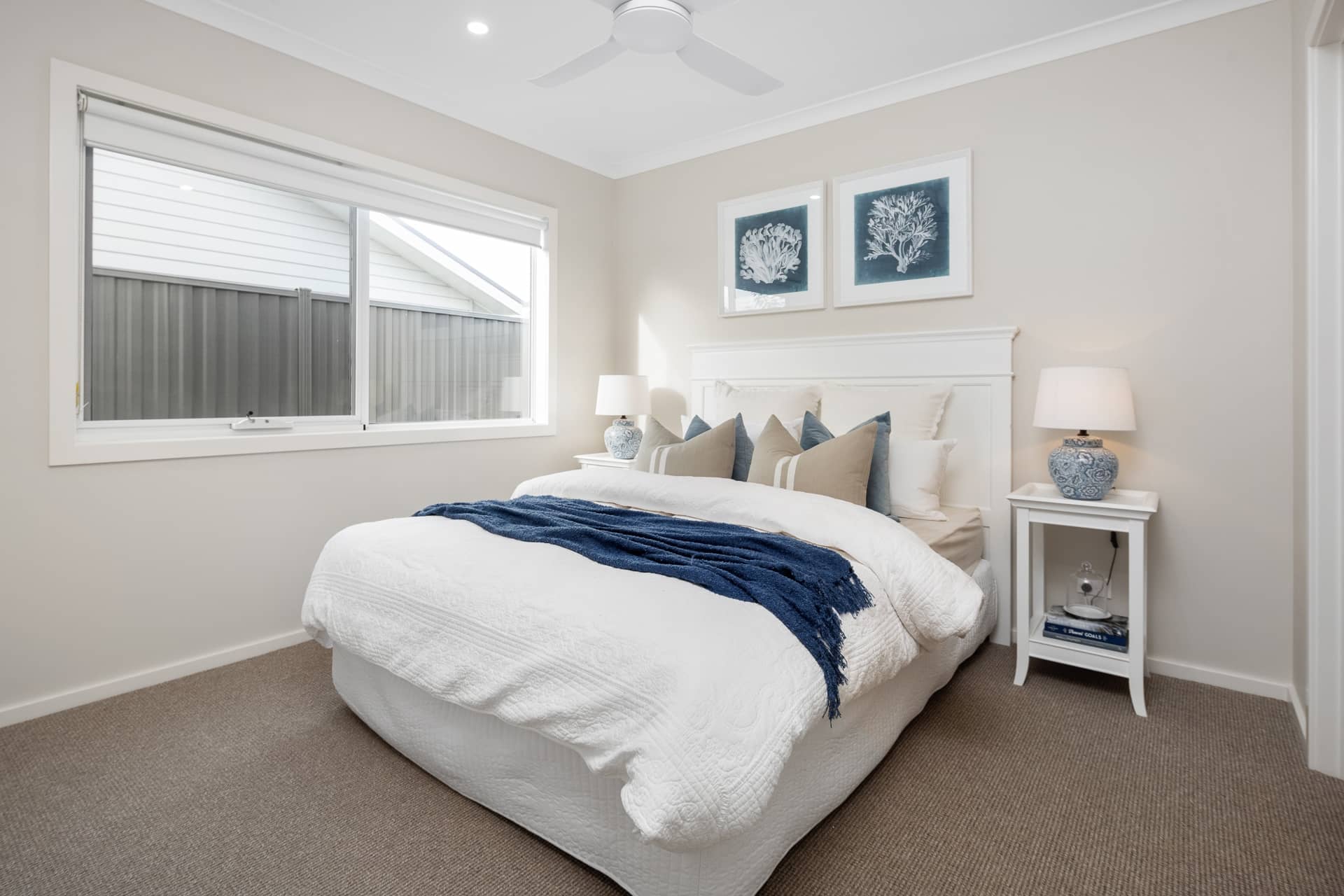 Bedroom with white bed, blue throw blanket, and coastal-themed artwork.