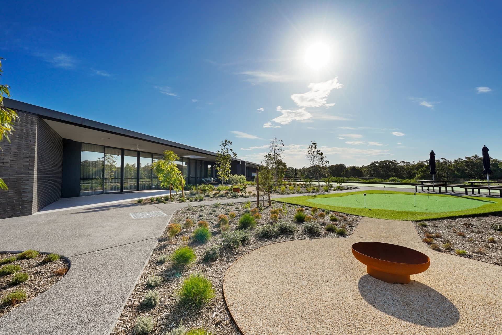 Ingenia Lifestyle community's modern clubhouse, putting green, fire pit, and landscaped gardens on a sunny day.