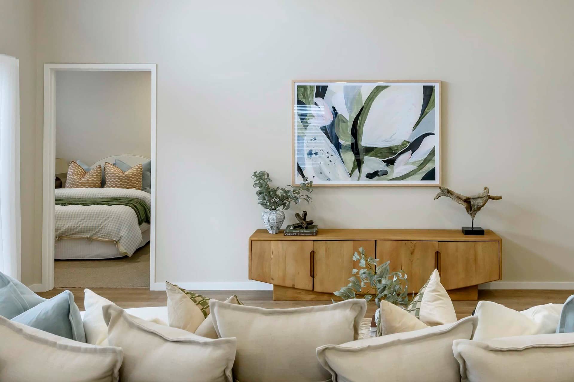 A spacious living room with a hallway view into a bedroom, featuring a modern wooden sideboard and abstract art.