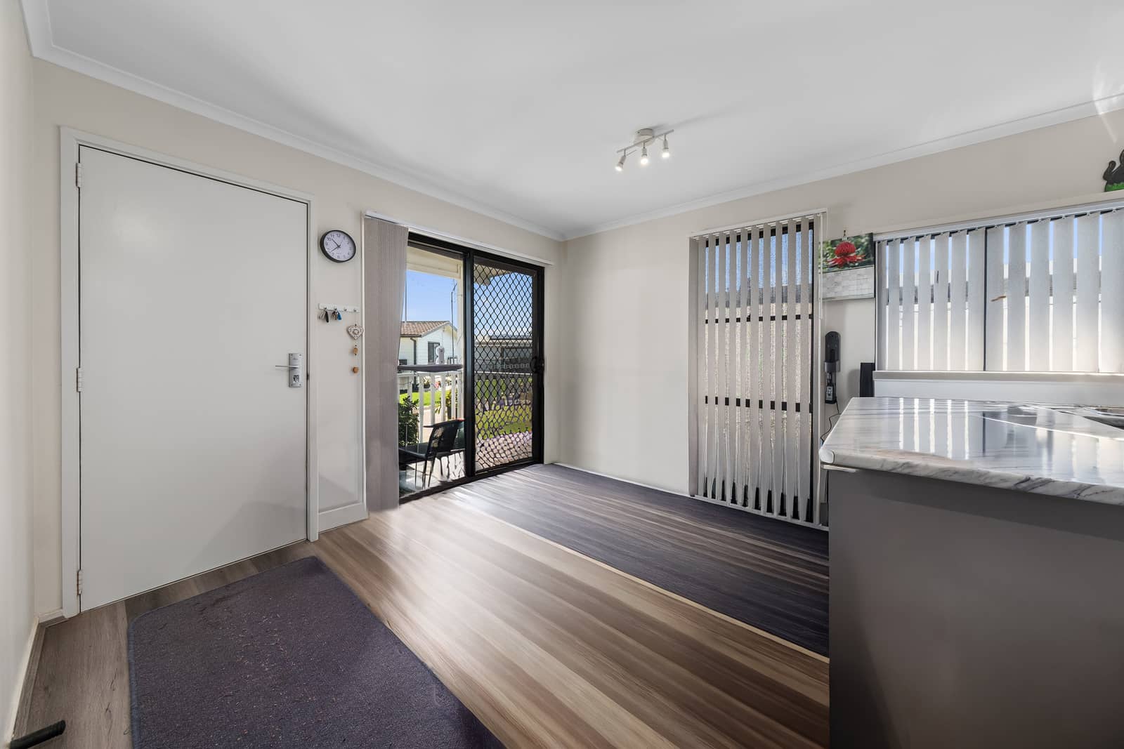 Interior view of a room with wood-look flooring, a white door, a sliding glass door to a patio, and a kitchen benchtop.
