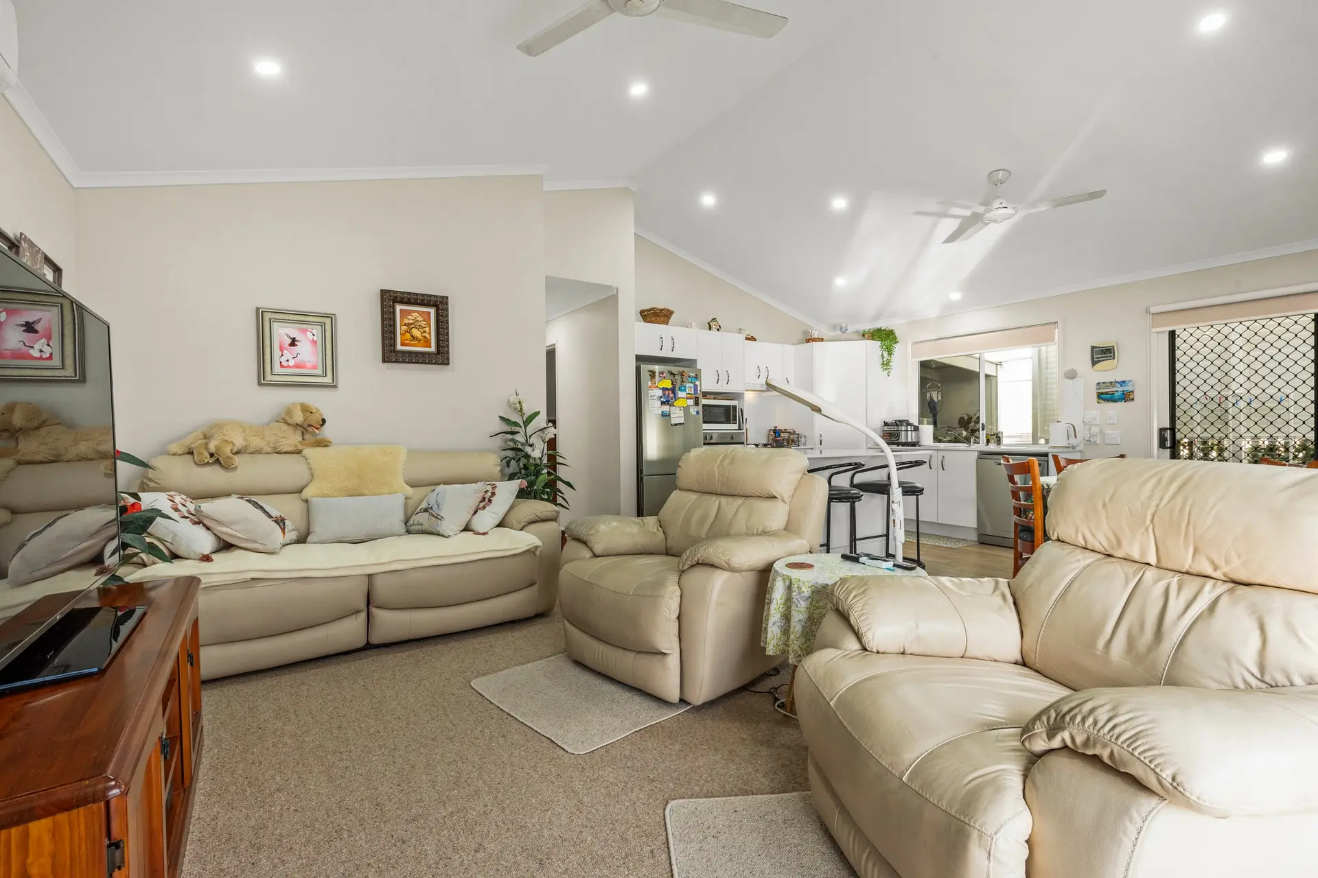 Open plan living room and kitchen in an Ingenia Lifestyle home with beige leather sofa, recliner, and white kitchen cabinetry.