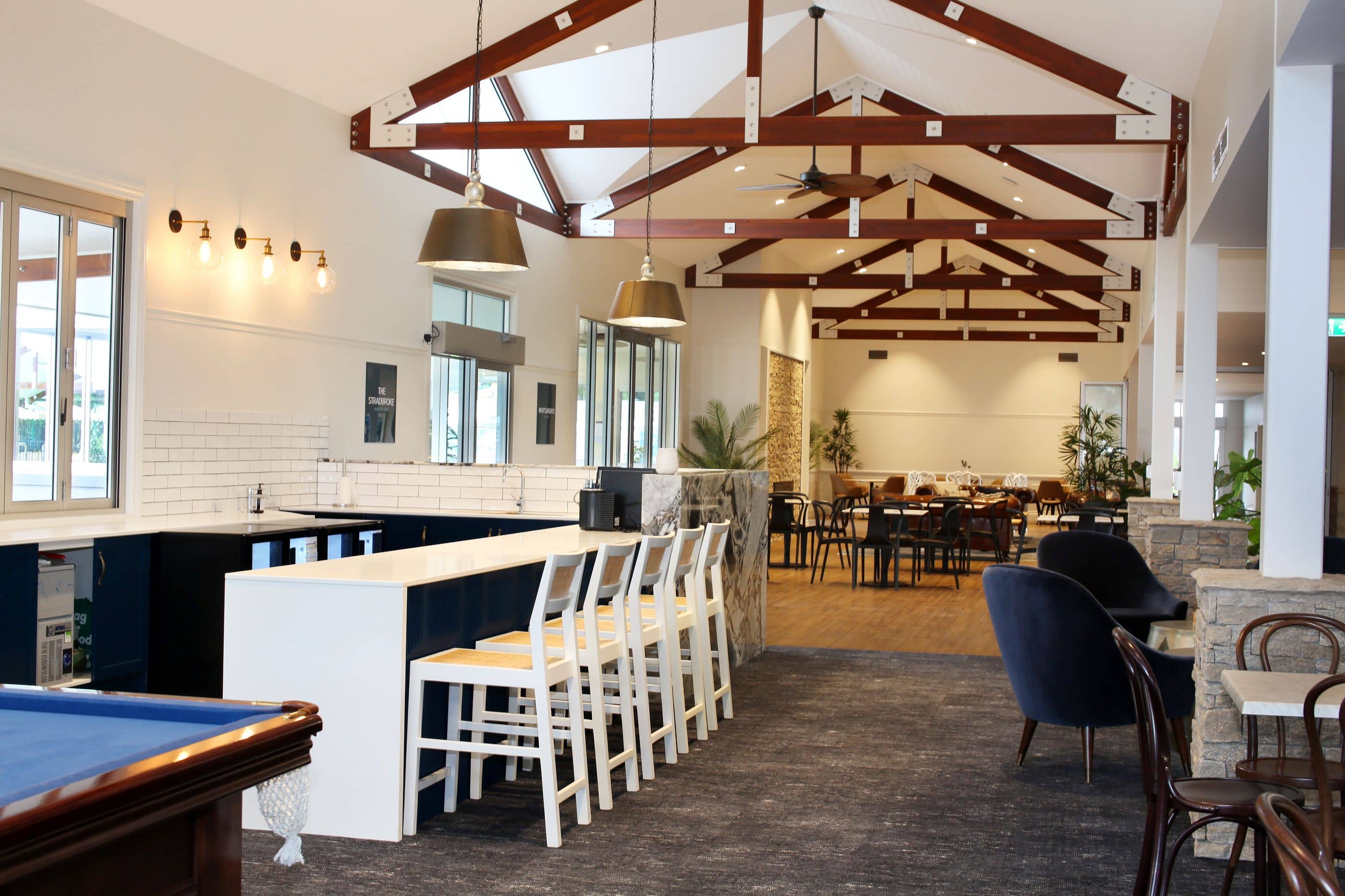 Interior of a community lounge with a bar, pool table, seating area, and dining tables.