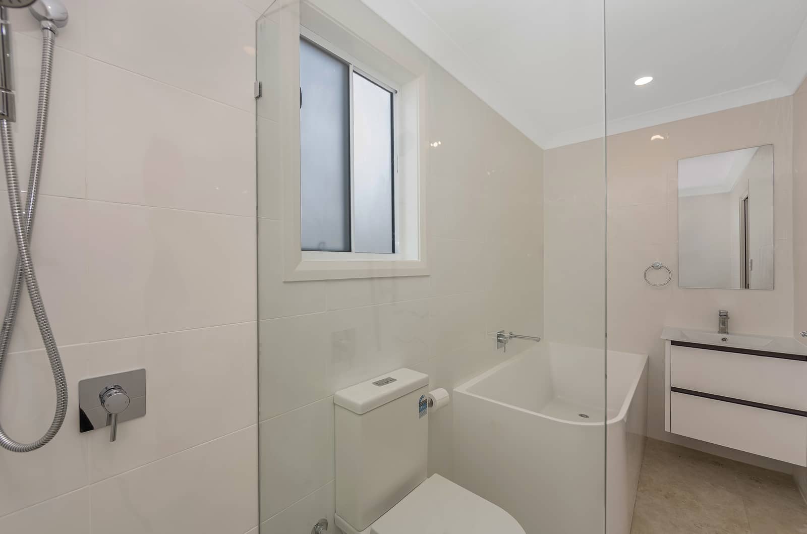 A light-toned bathroom featuring a shower, toilet, compact bath, window, and vanity with mirror, in an Ingenia Lifestyle home.