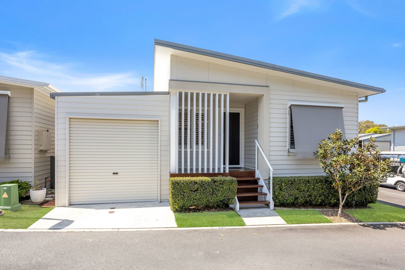 Modern light-colored Ingenia Lifestyle home with an attached garage, porch with steps, and low-maintenance landscaped grounds.