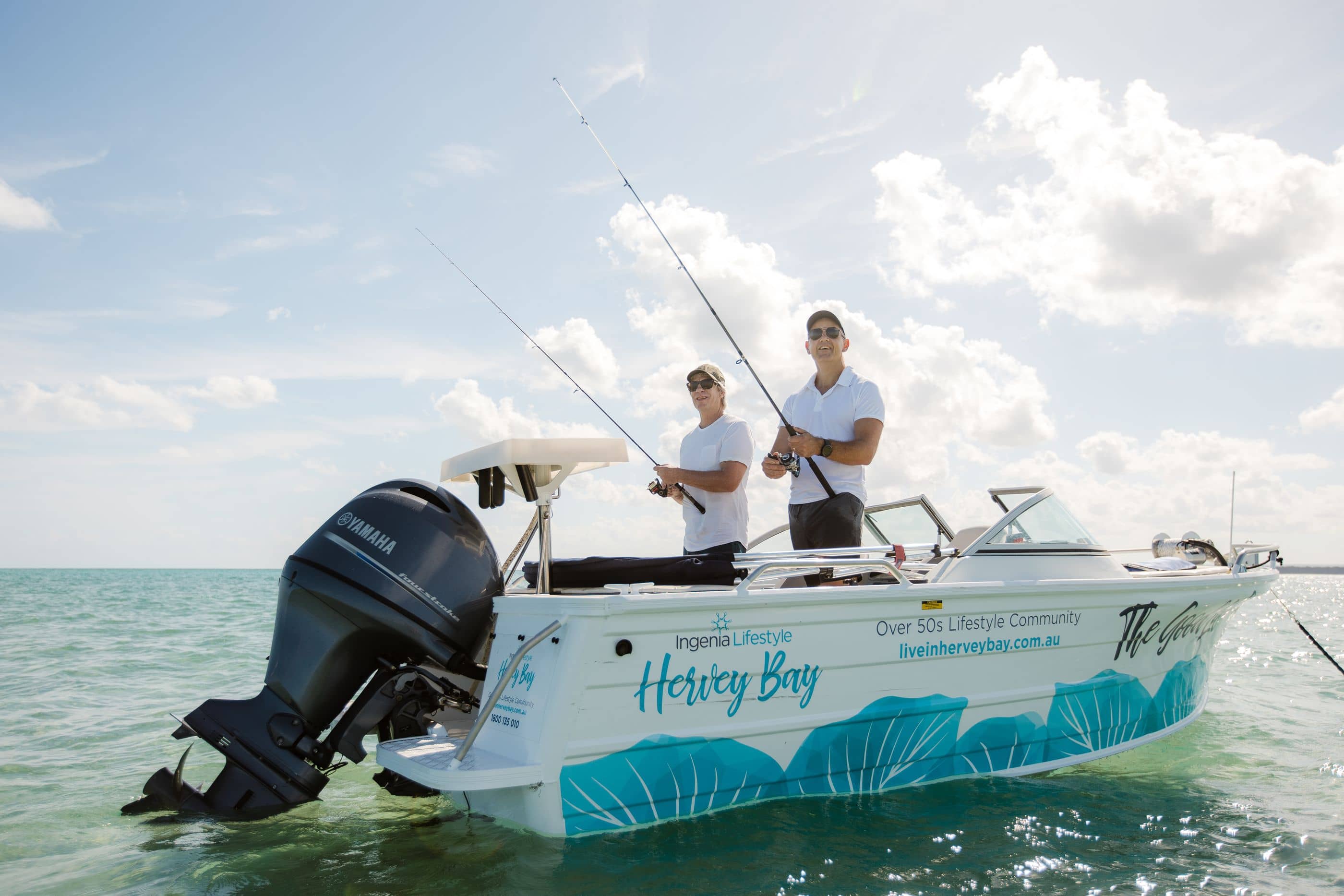 Two men fishing from a boat in the ocean, with "Ingenia Lifestyle Hervey Bay" branding visible.
