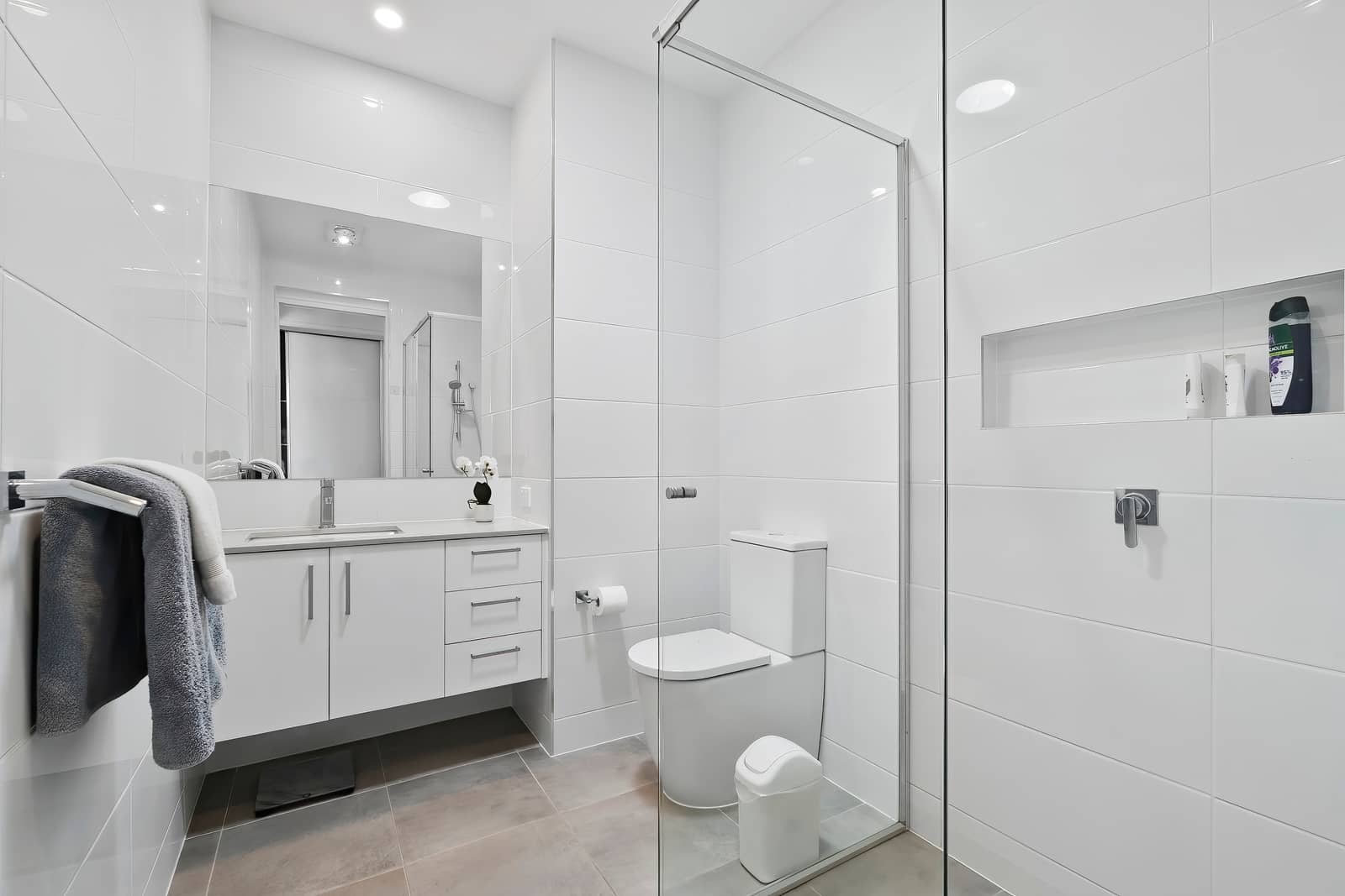 Clean, white-tiled bathroom in an Ingenia Lifestyle home with a vanity, mirror, toilet, and glass-screened shower.
