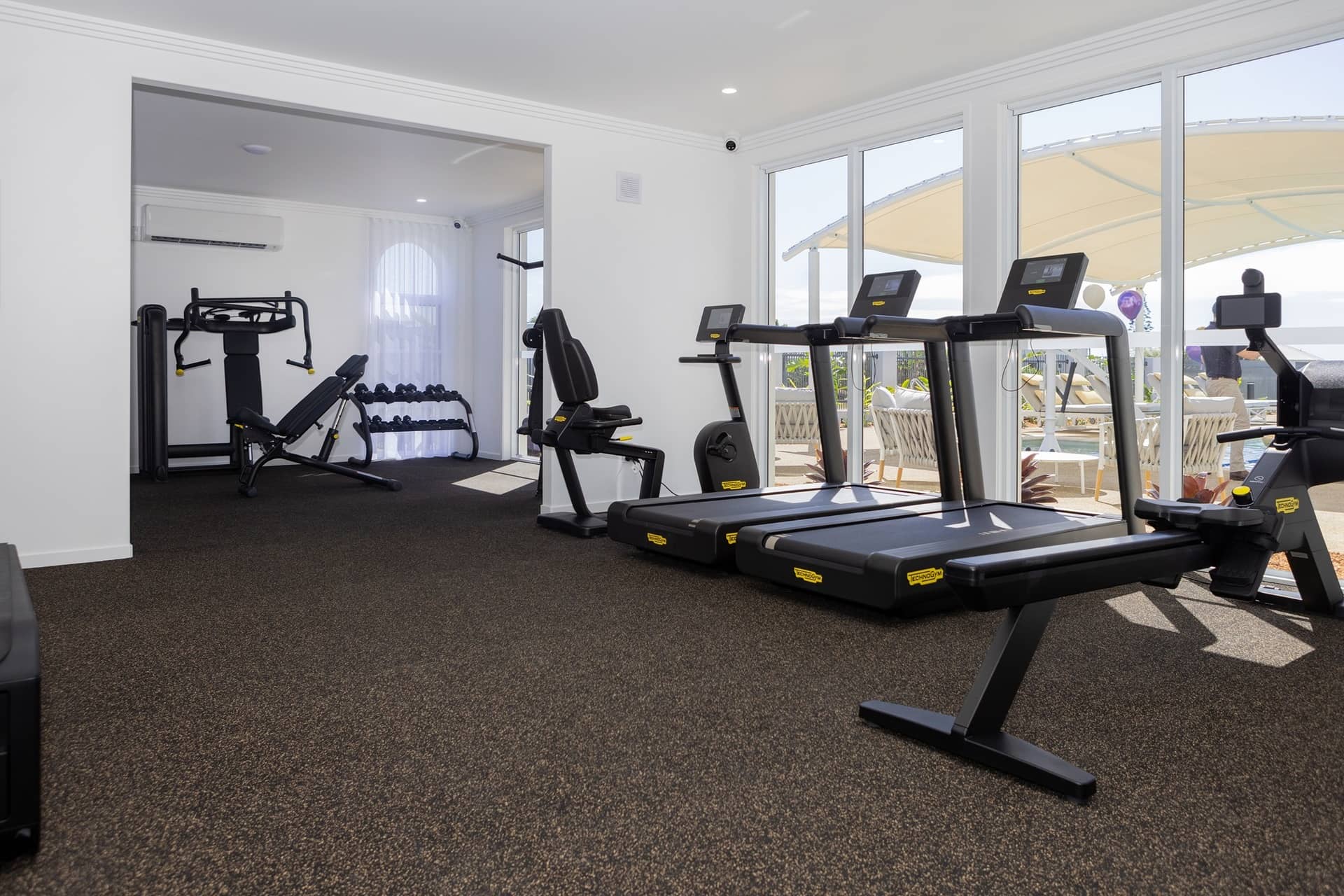 Ingenia Lifestyle community gym with treadmills, recumbent bike, weight machine, and dumbbells.