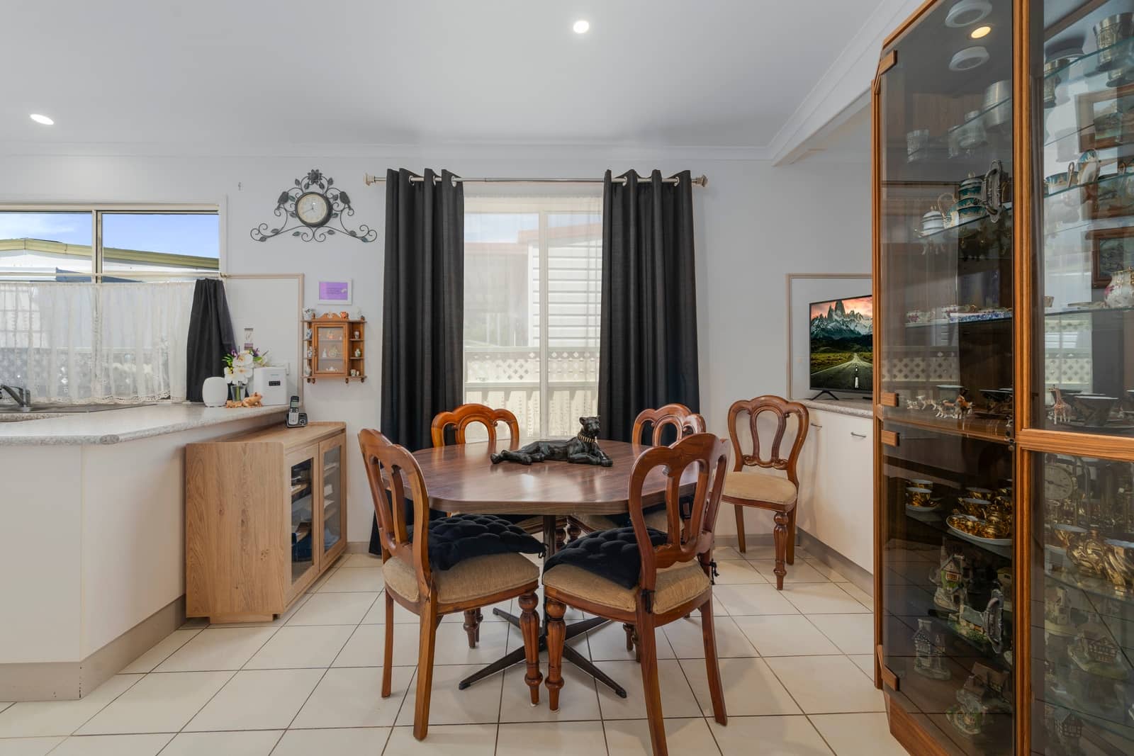 Dining area of an Ingenia Lifestyle home with an oval wooden table, six chairs, and a decorative panther statue. Adjacent kitchen and a glass display cabinet.