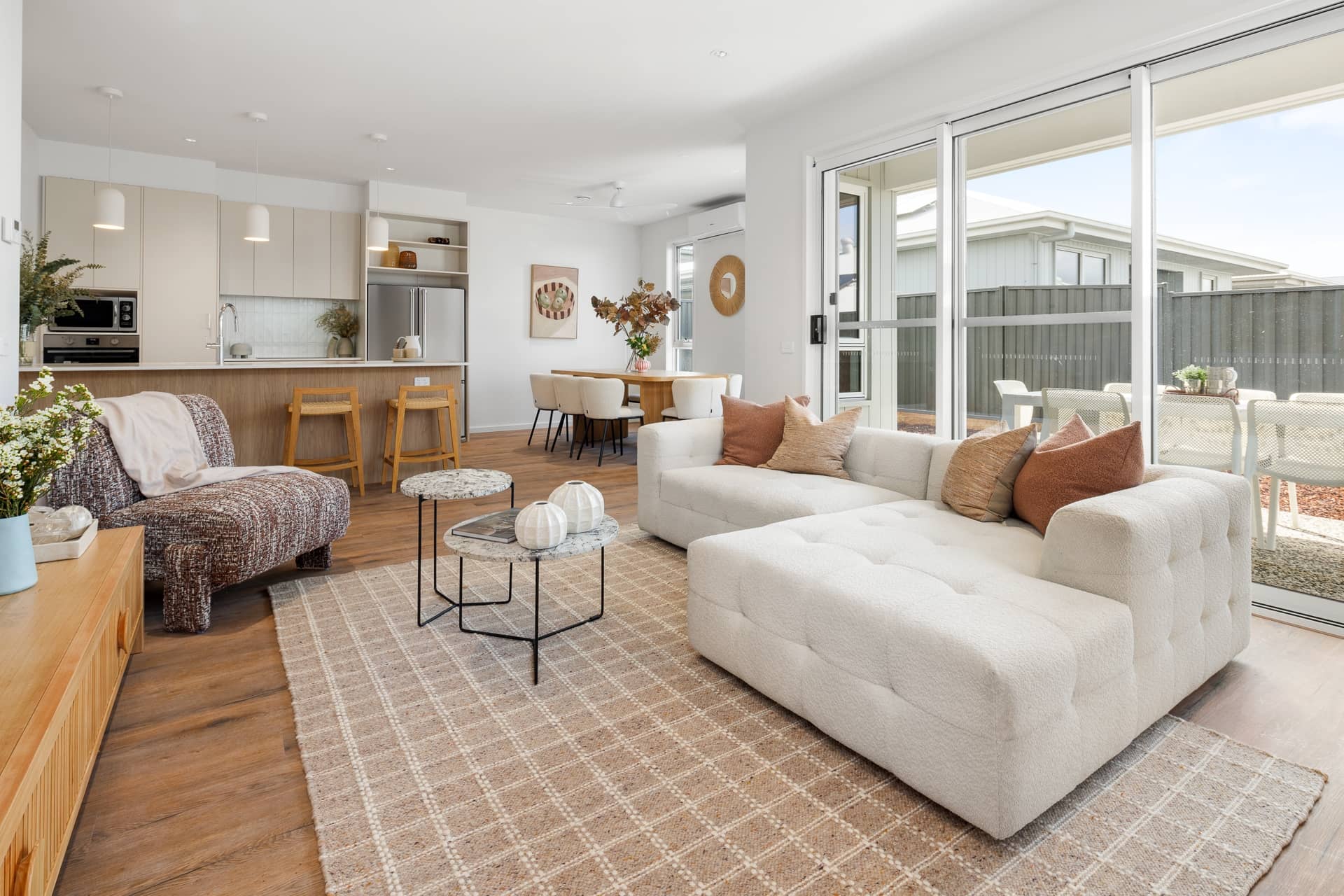 A spacious, open-plan living area and kitchen with a light sofa, dining table, and glass doors opening to an outdoor patio in an Ingenia Lifestyle home.