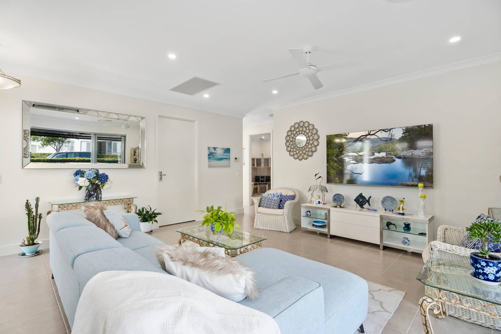 A bright living room in an Ingenia Lifestyle home with a blue sectional sofa, TV, and modern white furniture.