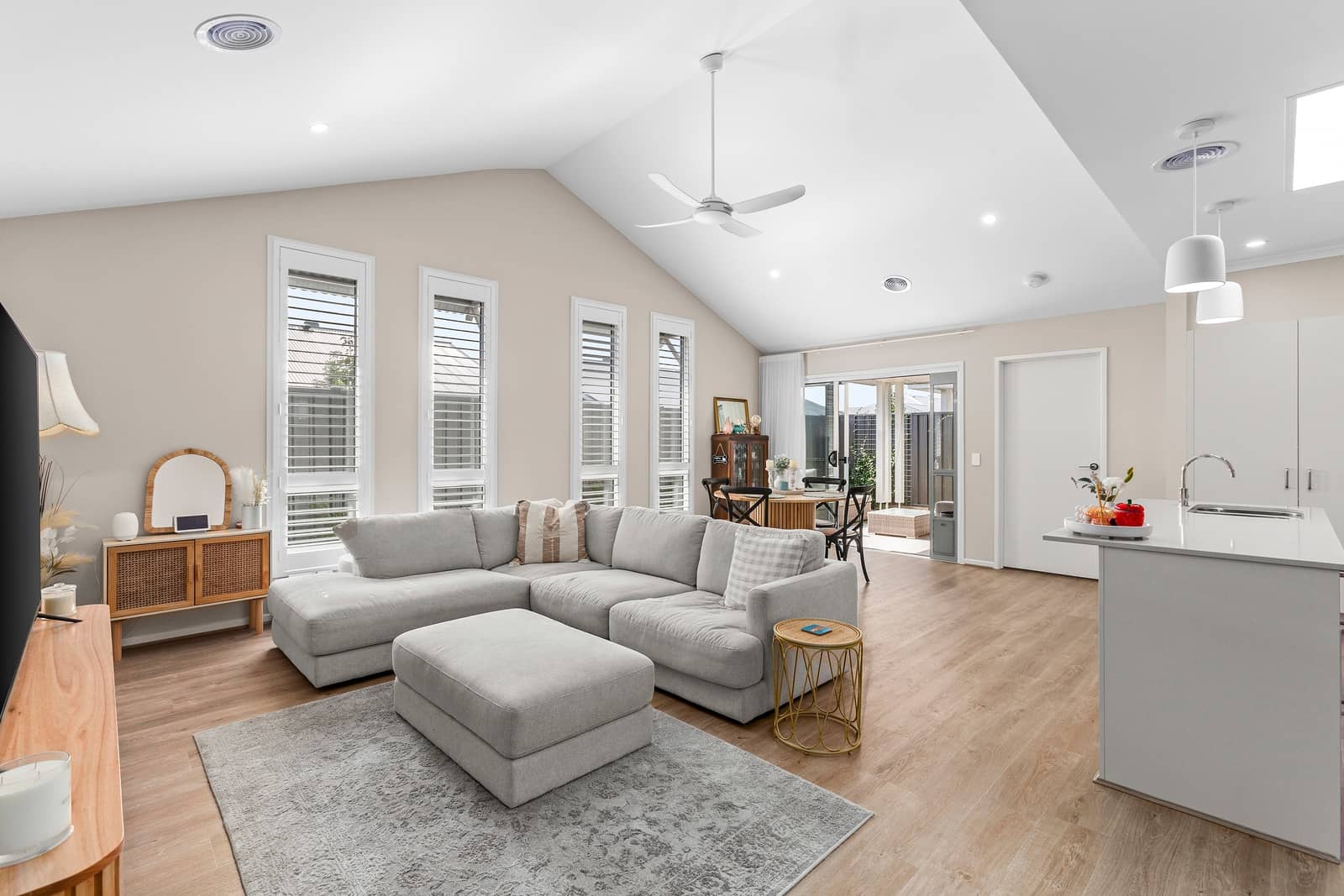 Light-filled open-plan living area in an Ingenia Lifestyle home, featuring a grey sofa, wood floors, and vaulted ceilings.