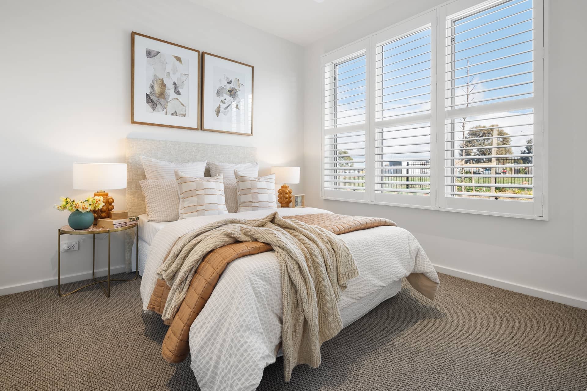 Bedroom in an Ingenia Lifestyle home with a bed, neutral bedding, bedside tables, and large windows with white shutters.