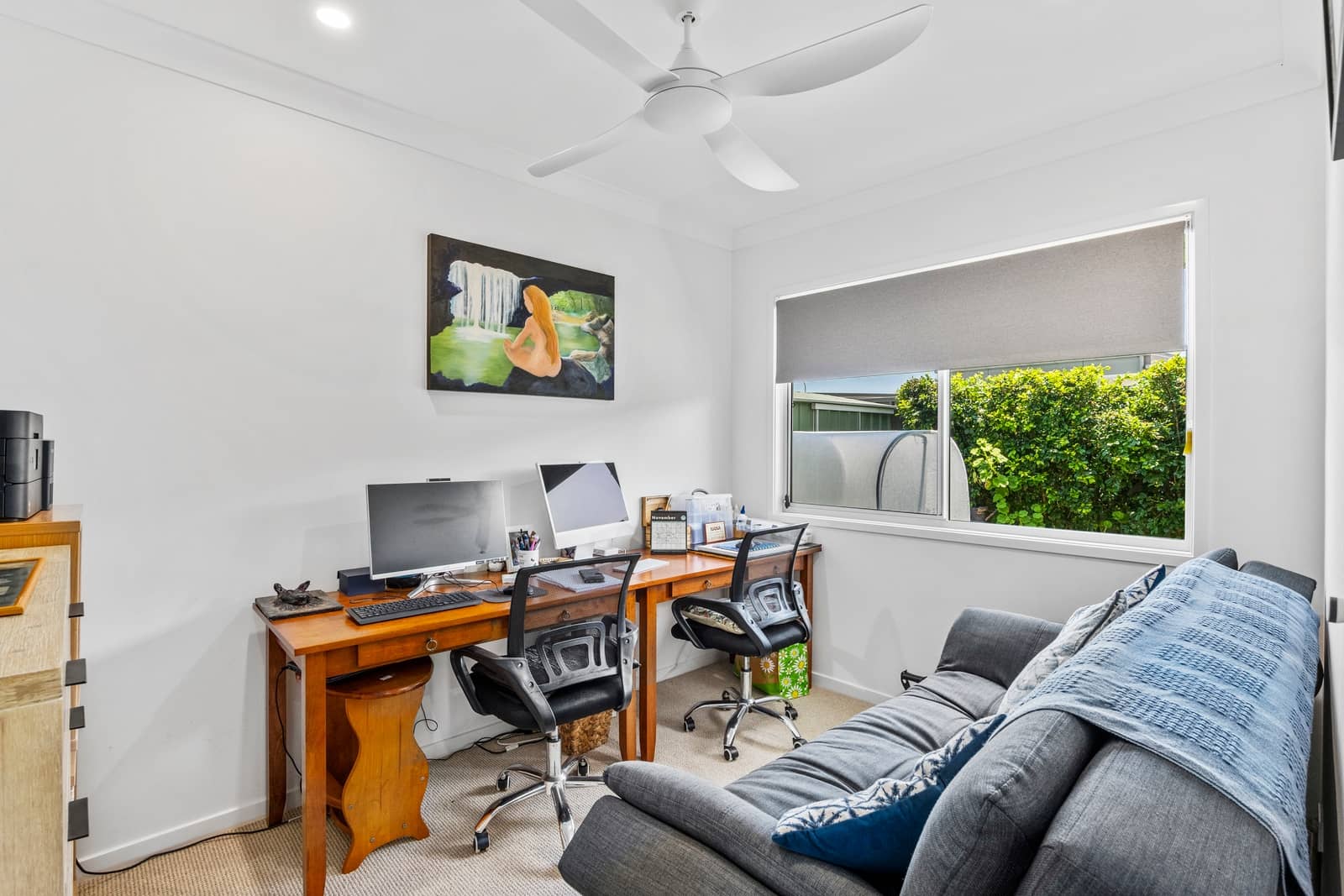 A flexible home office in an Ingenia Lifestyle home, with a double desk, computers, sofa, and window views of landscaped grounds.