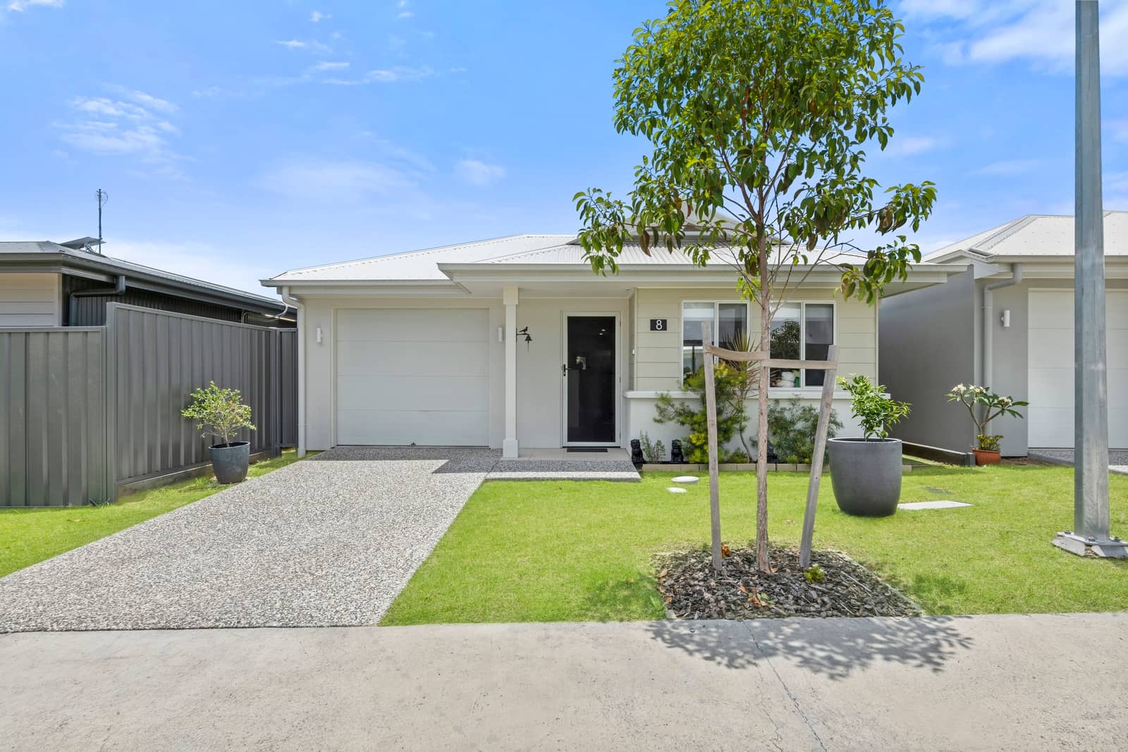 Modern Ingenia Lifestyle land-lease home with white garage door, light facade, green lawn, and a young tree.