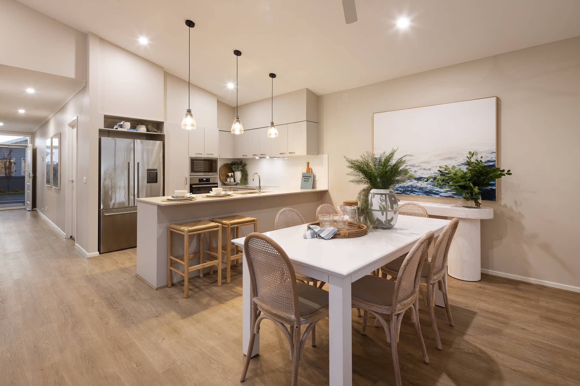 A modern dining and kitchen area with a white table, cane chairs, and a kitchen island with stools.
