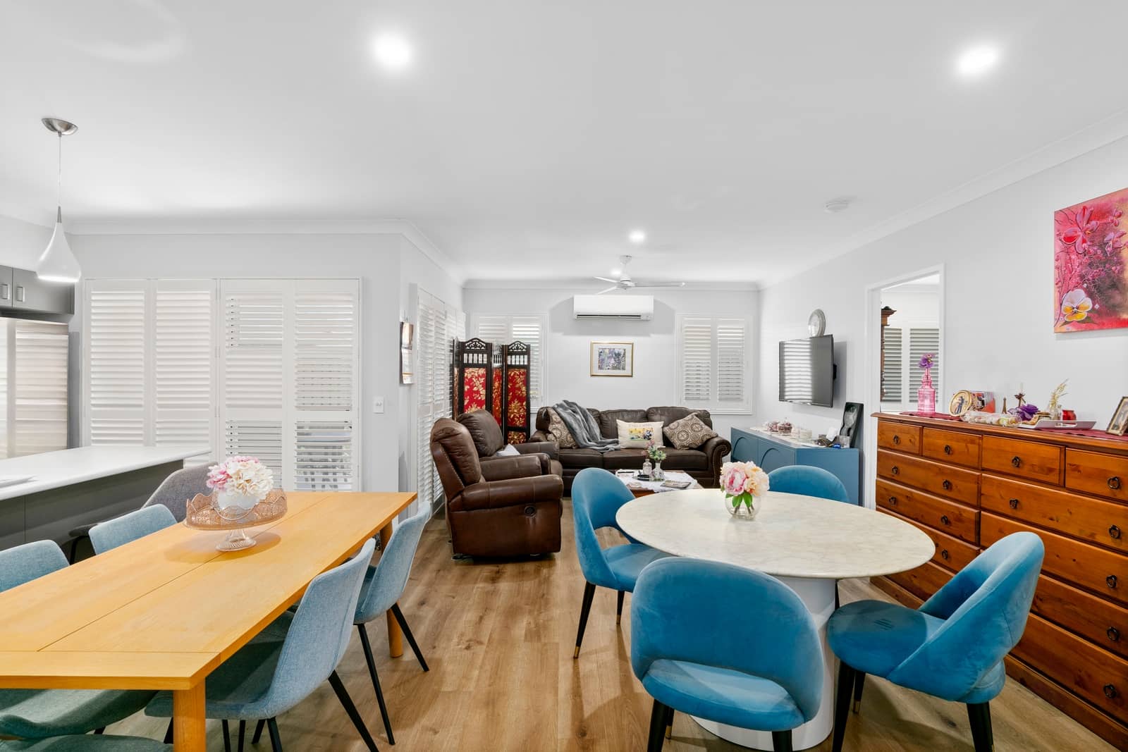 Interior view of a living and dining area in an Ingenia Lifestyle community, showing two dining tables with chairs, a lounge suite, and a wooden dresser.