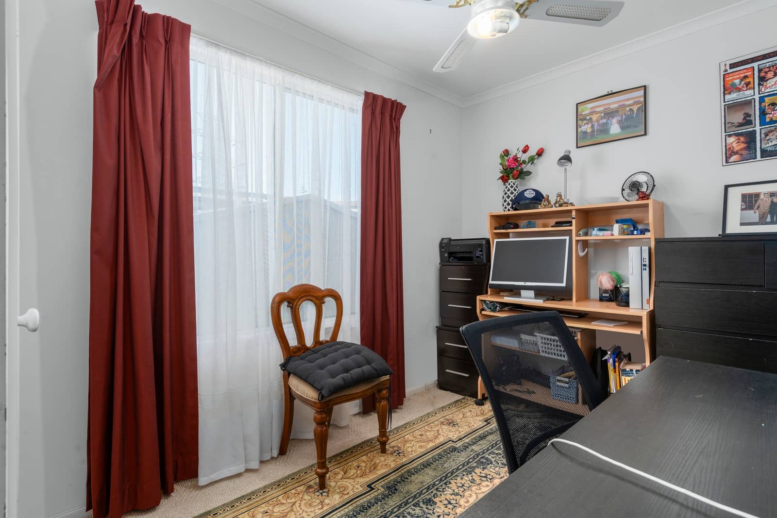 Home office in an Ingenia Lifestyle home with a desk, computer, printer, window with curtains, ceiling fan, and rug.