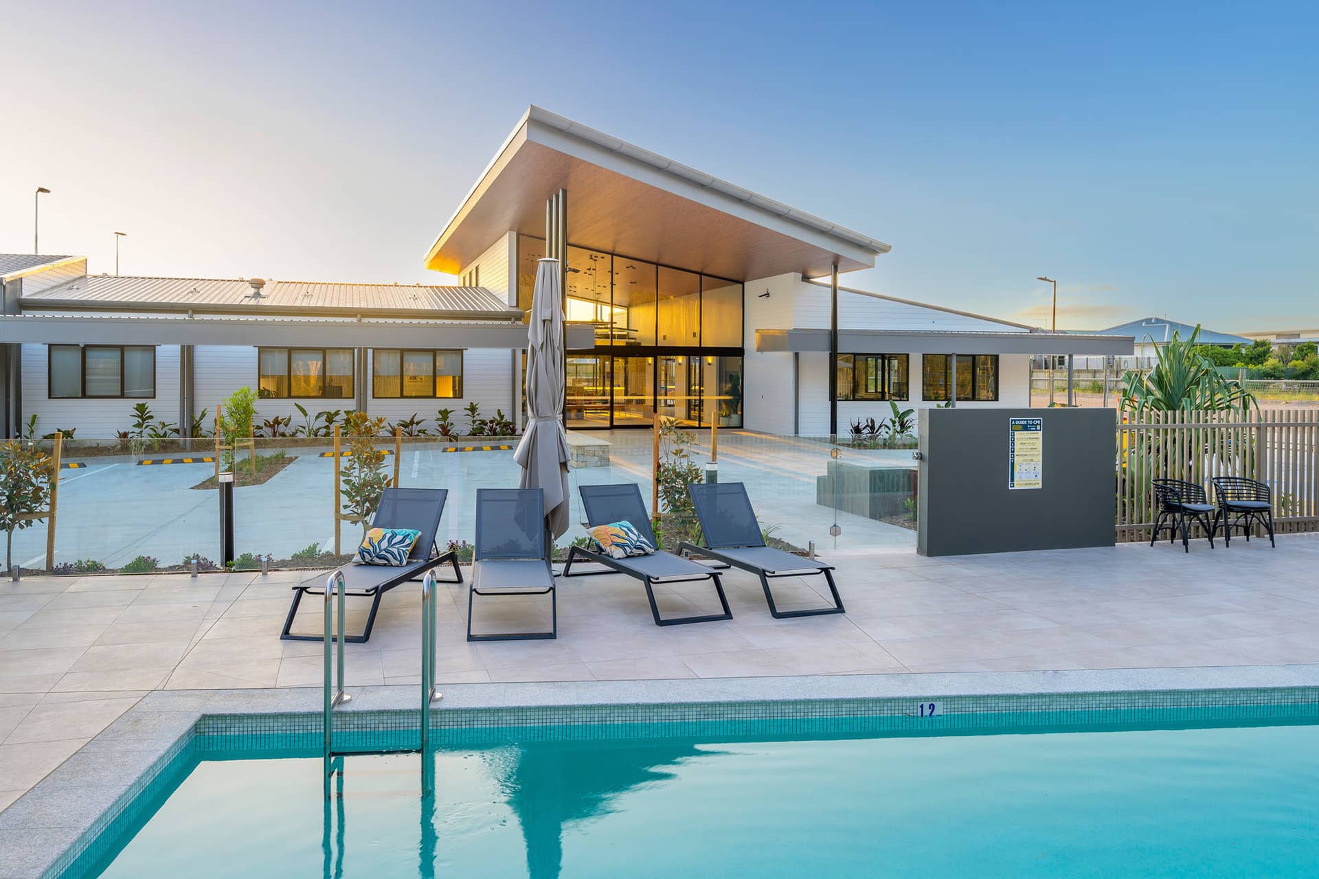 Modern Ingenia Lifestyle community building with glass windows, a shared swimming pool, sun loungers, and paved deck.