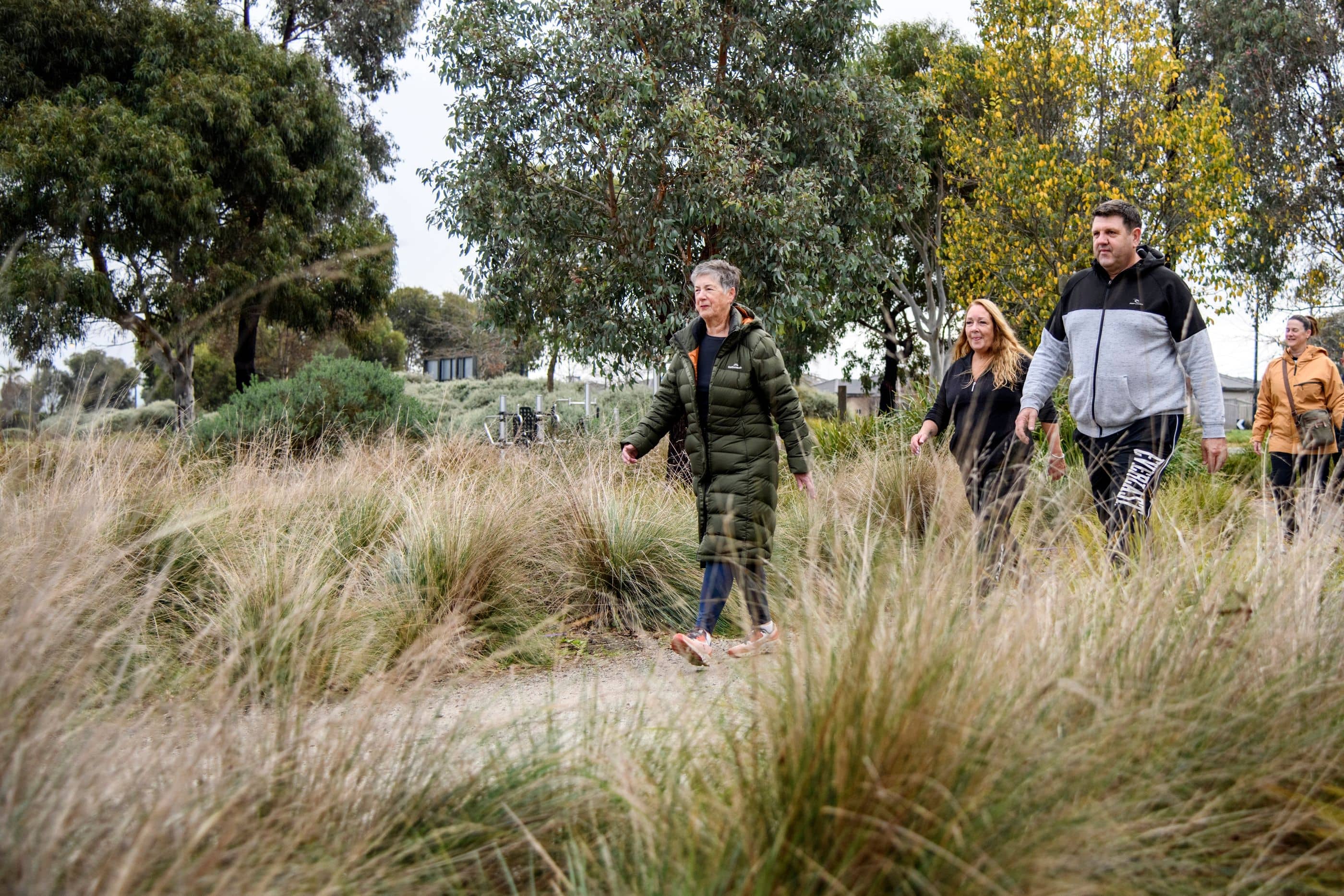 People walk on a path through tall grasses and trees in an Ingenia Lifestyle community.