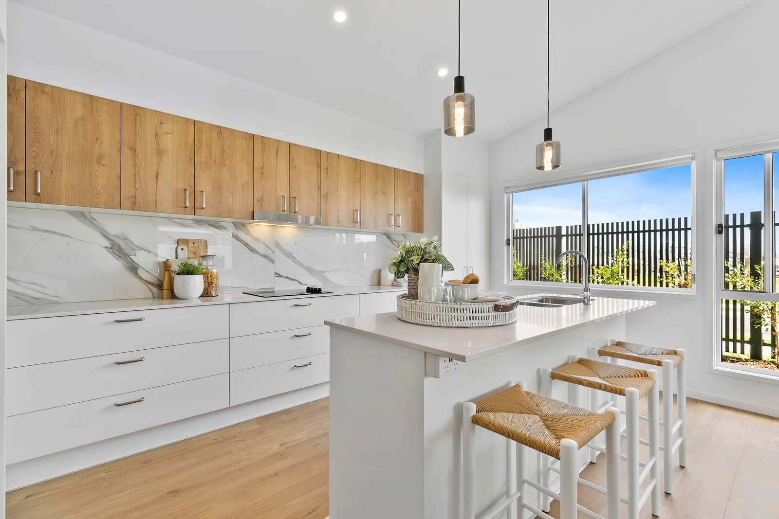 Modern Ingenia Lifestyle kitchen featuring white and timber-look cabinets, marble-patterned splashback, island, and large window.