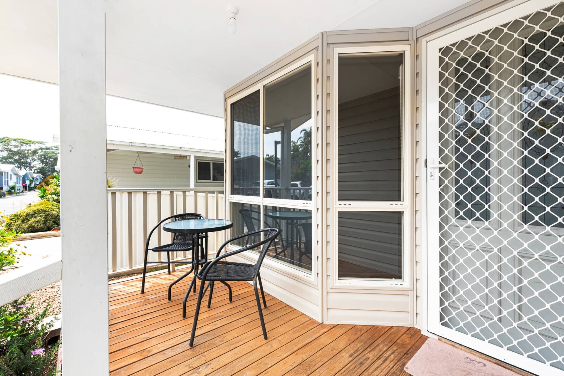 A wooden deck with a small outdoor table and two chairs in front of a land lease home in an Ingenia Lifestyle community.