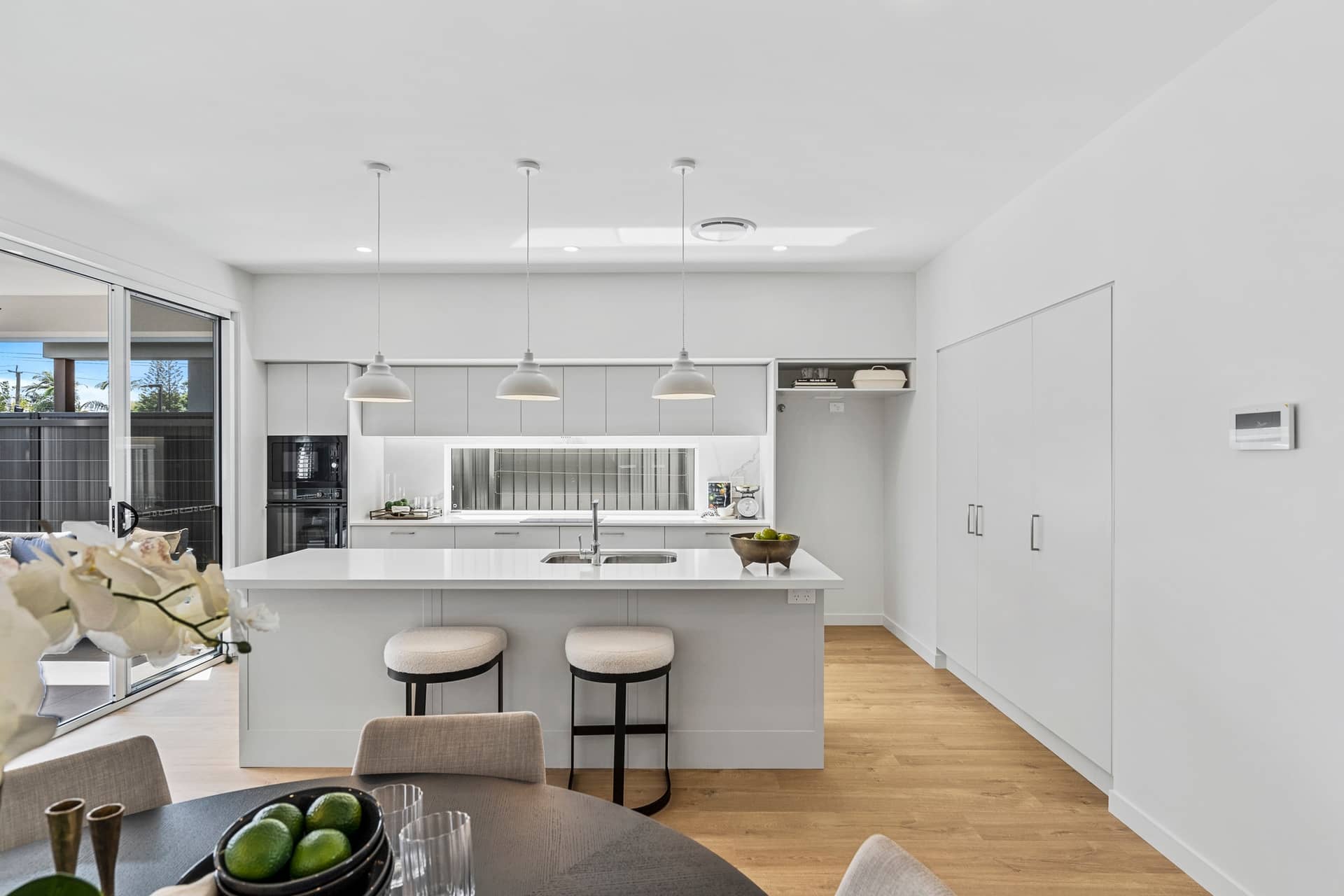 Modern light grey kitchen with a large island, pendant lights, and a dining area in the foreground.