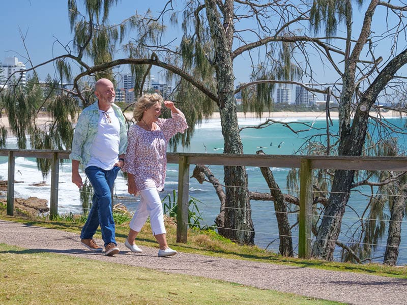 Over 50s couple walking along path next to Sunshine Coast beach - Ingenia Lifestyle Nature's Edge